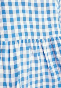 Blåt og hvidt gingham-stof har et ternet mønster med forskellige blå nuancer. Det har en tekstureret overflade og samling med rynkede detaljer.