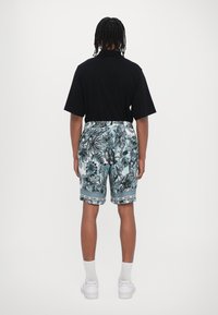 Maglietta nera a maniche corte abbinata a pantaloni corti leggeri azzurri con un design di fogliame tropicale, vita elastica e rifiniture blu.
