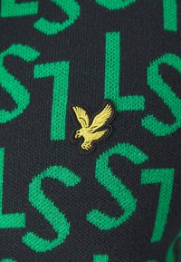 Tessuto nero lavorato a maglia con grandi lettere verdi e un logo di aquila ricamato giallo su uno sfondo nero.