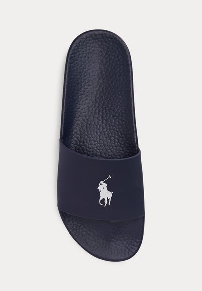 Σανδάλι σλάιντ σε ναυτικό μπλε με υφή στο πέλμα και λευκό λογότυπο παίκτη πόλο σε φαρδιά λουρίδα, εμφανιζόμενο από πάνω, σε λευκό φόντο.