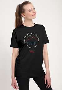Sort bomulds t-shirt med en hvid, rød og blå grafik af bjerge og en sol, med teksten "Durham Mountaineering Since 1981".