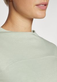 Lys grønn sweatshirt med en glatt bomullstekstur, med rund hals og subtile sømdetaljer langs brystet.
