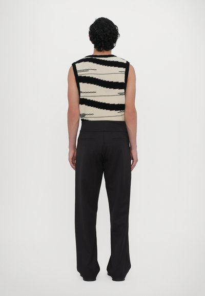 Top sem mangas de malha com padrão zigzag em preto e creme; combinado com calças largas pretas, tecido suave, com detalhes mínimos.