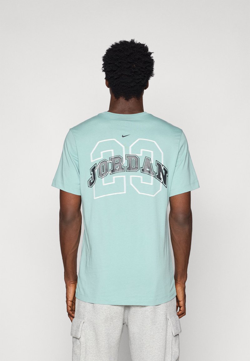 Camiseta de algodón verde claro con la inscripción "JORDAN" y "23" en letras grises y blancas en la parte posterior, con un logo de Nike encima. Manga corta.