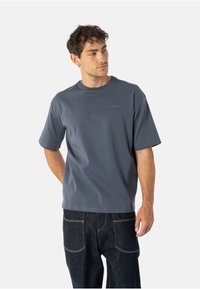 Krótki rękaw ciemnoszary T-shirt z okrągłym dekoltem, gładką fakturą i subtelnym logo na piersi, zestawiony z ciemnymi dżinsami.