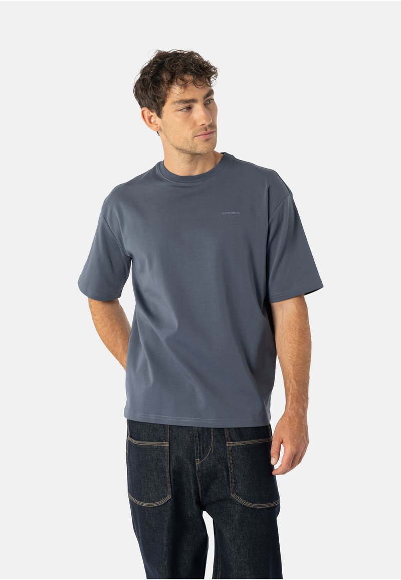 Krótki rękaw ciemnoszary T-shirt z okrągłym dekoltem, gładką fakturą i subtelnym logo na piersi, zestawiony z ciemnymi dżinsami.