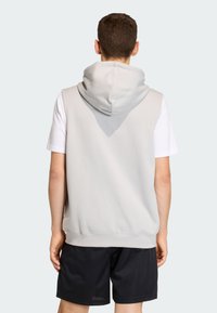 Svetlosivá tielková mikina s veľkou kapucňou, mäkkou textúrou a rebrovaným lemom, nosená cez biele tričko s krátkym rukávom, skombinovaná s čiernymi šortkami.