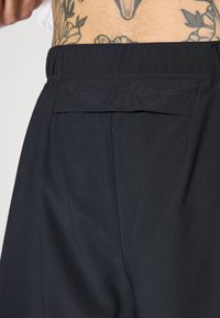 Shorts de sport noirs avec une texture lisse, une taille élastique et une poche arrière avec un détail de couture soigné.