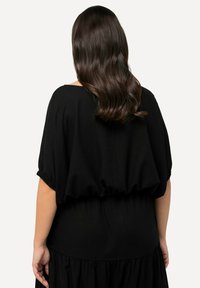 Robe noire caractérisée par une coupe décontractée, des manches courtes bouffantes et une taille froncée. Le tissu semble léger et lisse avec une jupe fluide.