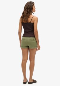 Débardeur marron à fines bretelles, shorts verts et sandales à glissière marron. Les shorts sont dotés de poches arrière et d'un ourlet roulé.