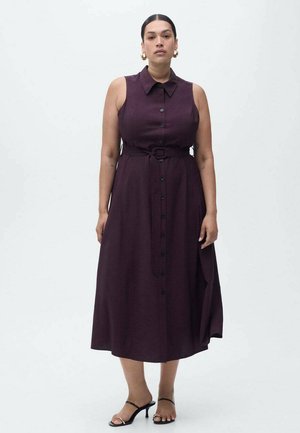 Une robe sans manches, violette foncée, avec un col, un bouton à l'avant, une taille ceinturée et une jupe fluide. Des sandales noires sont portées.