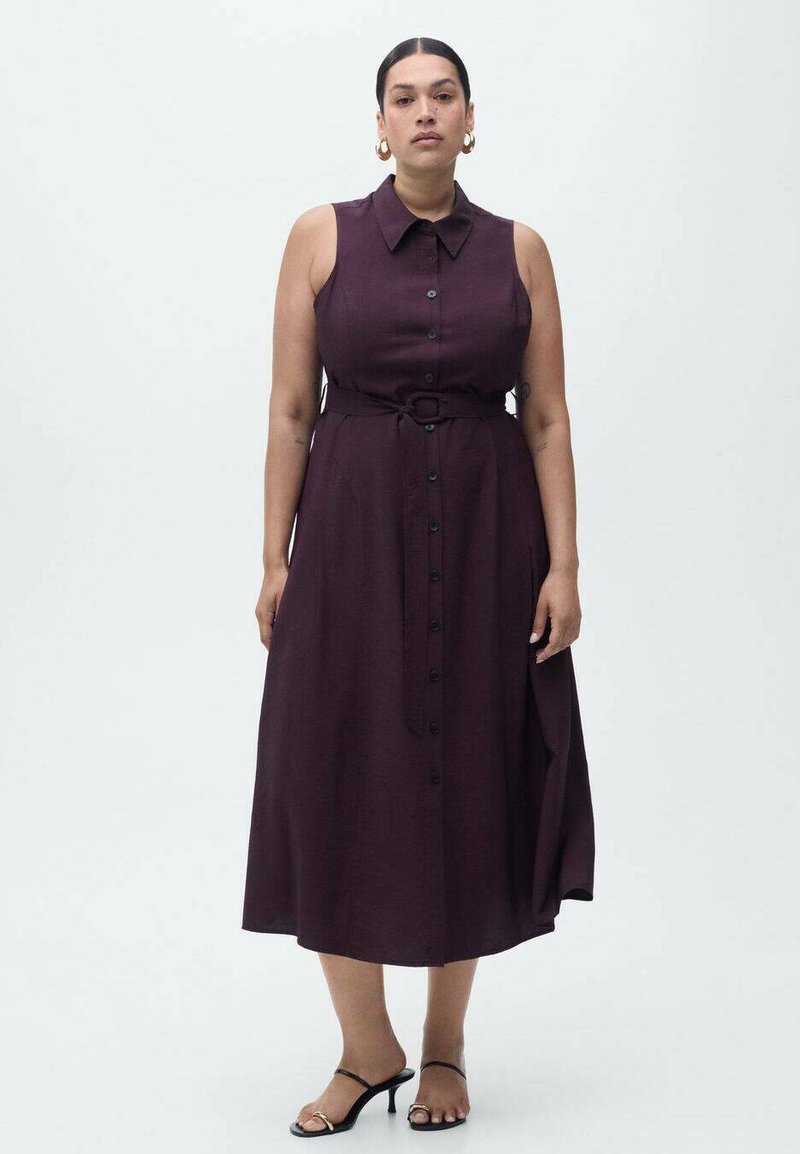 Un vestito senza maniche di un viola scuro, con colletto, chiusura frontale a bottoni, vita con cintura e una gonna fluente. Sono indossati sandali neri.