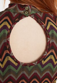 Nahaufnahme eines mehrfarbigen, gemusterten Kleidungsstücks mit Chevron-Design, das einen runden Ausschnitt auf der Rückseite und zwei Knopfverschlüsse aufweist.
