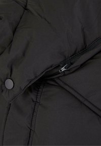 Schwarze Daunenjacke mit diagonaler Steppung, mattem Stoff, seitlichem Reißverschluss und Druckknopfdetail.