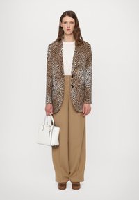 Blazer en imprimé léopard, haut crème, pantalon beige taille haute, sac à main blanc, chaussures marron, texture lisse, coupe oversize, design épuré.