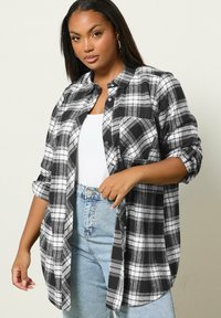 Svartvitt rutigt flanellskjorta med knäppning, med uppvikt ärmar och en bröstficka. Bärs över en vit topp.