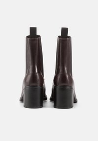 Botas de tornozelo em couro castanho com um salto quadrado, painéis laterais elásticos e um acabamento elegante. O design é moderno, com um perfil minimalista.