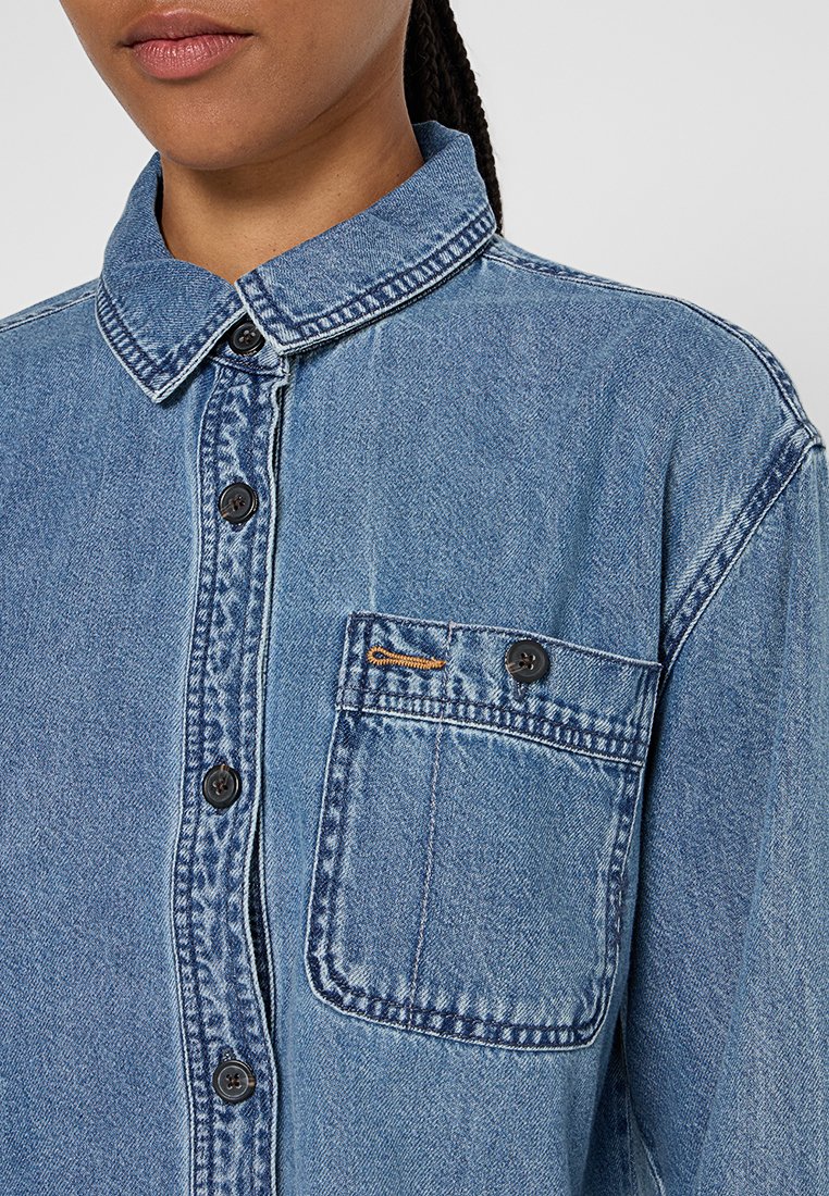 Lichtblauwe denim overhemd met een kraag, borstzak en zwarte knopen. Opvallende vervaging en stikseldetails.