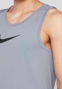 Camiseta deportiva gris sin mangas con cuello redondeado, amplias sisas y un logo negro de Nike en el pecho, hecha de tela transpirable.
