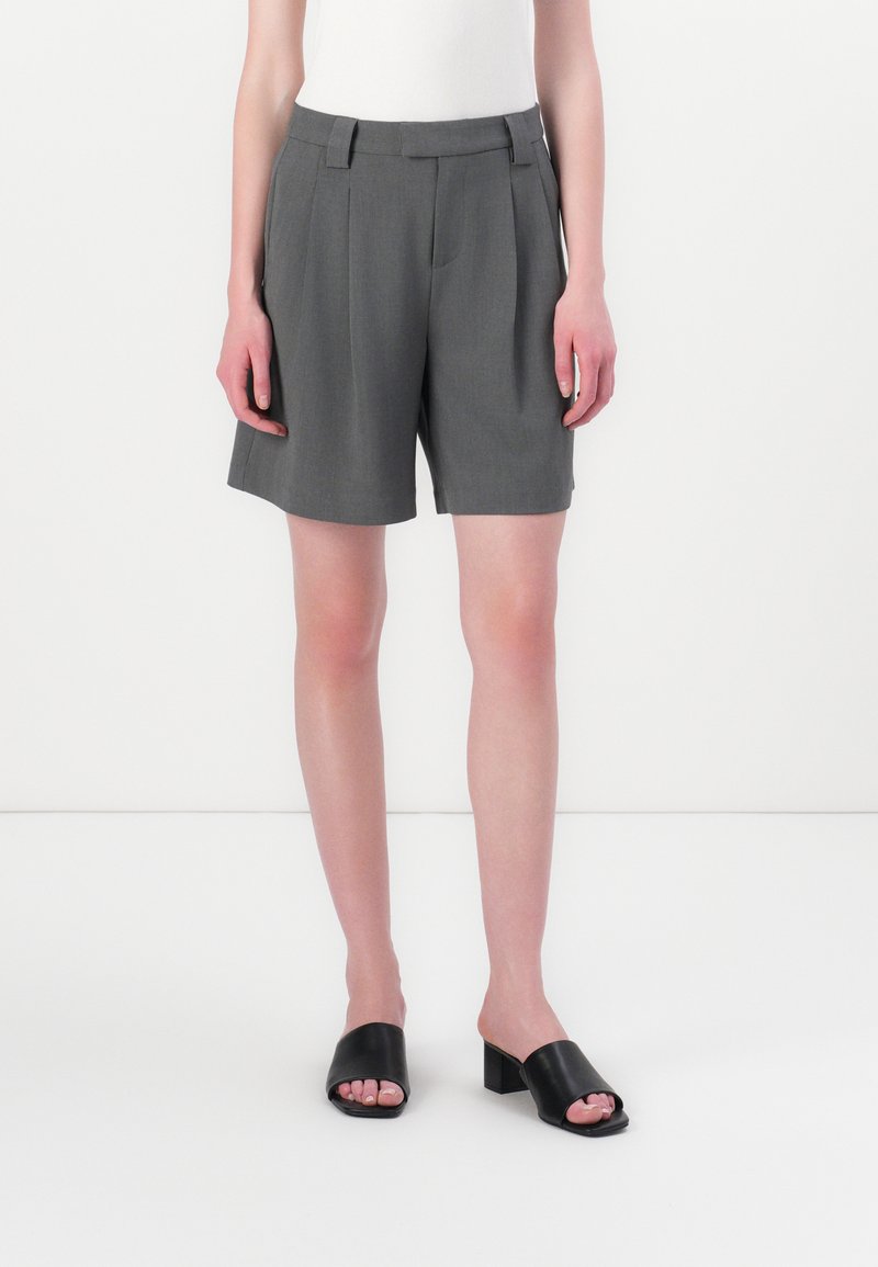 Grå skreddersydde shorts med frontfolder, rett snitt og beltehemper, paret med svarte åpne tå blokkhæl sandaler.
