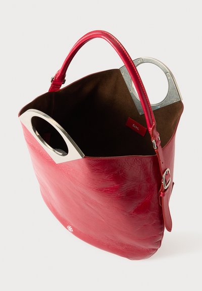 Sac à main en cuir rouge avec une texture lisse, un design semi-structuré et une anse circulaire en argent. L'intérieur est doté d'une doublure en suède marron.