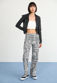 Cropped black jacket with gold zipper, white cropped top, and black and white patterned flared pants, paired with black and white sneakers.