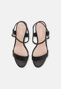 Schwarze Absatzsandalen mit einem glatten Lederoberteil, einem breiten Riemen über den Zehen und einem Knöchelriemen mit einer silbernen Schnalle.
