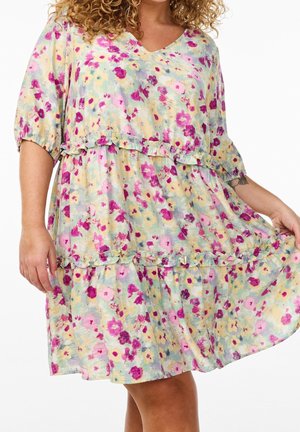 Woman wearing a loose, knee-length floral dress with pink, purple, and yellow flowers and ruffle details on the tiers and sleeves.