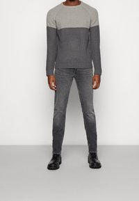 Grå stickad tröja med en ljusgrå överdel, parat med ljusgrå jeans och svarta skor med tjock sula. Slät textur genom hela plagget.