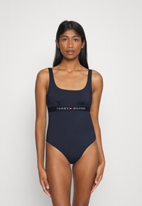 Costume intero navy con scollatura quadrata, spalline larghe e una fascia nera a contrasto con il logo "TOMMY HILFIGER" in vita.