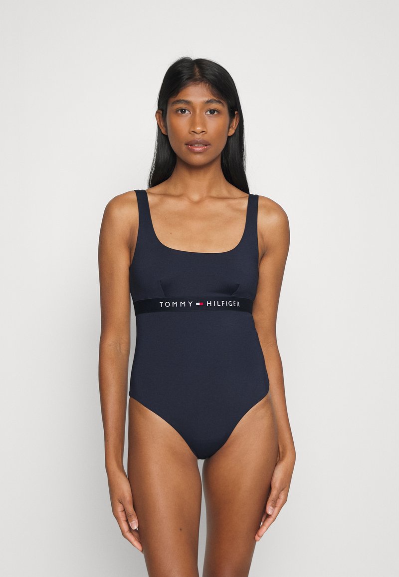 Costume intero navy con scollatura quadrata, spalline larghe e una fascia nera a contrasto con il logo "TOMMY HILFIGER" in vita.