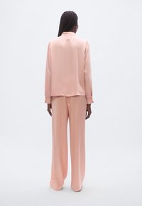 Lyserød satinbluse og bukser med vide ben, med lange ærmer med manchetter, glat tekstur og afslappet pasform, set bagfra.
