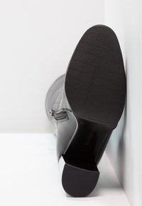 Botín de cuero negro hasta el tobillo con suela de goma texturizada, tacón afinado y detalle de cremallera lateral; acabado suave y acentos mínimos.
