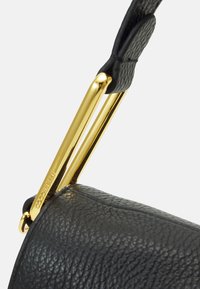 Borsa in pelle nera con una forma elegante e arrotondata. Presenta una maniglia in metallo dorato e un dettaglio del marchio inciso.