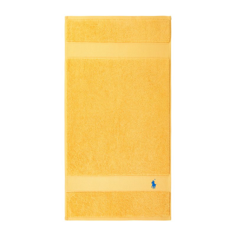 Κίτρινη βαμβακερή πετσέτα μπάνιου με πλούσια, υφή, που διαθέτει δύο οριζόντιες ταινίες και ένα μικρό μπλε λογότυπο κοντά στο κάτω μέρος.