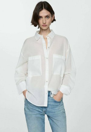 White, semi-transparent button-up shirt with two chest pockets, relaxed fit, and rolled cuffs, paired with light blue jeans.