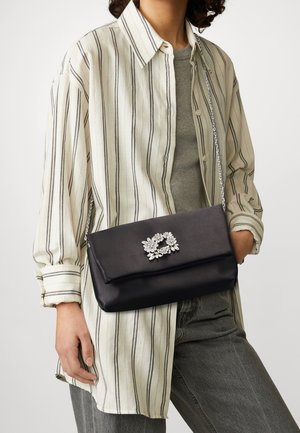 Zwarte satijnen clutch met een metallic kettingband, voorzien van een zilveren bloemenbroche aan de voorkant. Draagt met een gestreept shirt.