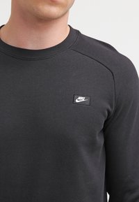 Svart Nike-tröja med texturerad tyg, ribbad rund halsringning och en liten, rektangulär logotyp på bröstet.