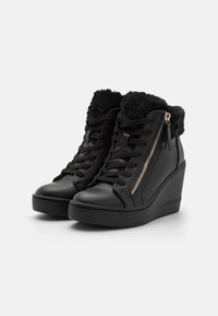 Baskets compensées noires avec col en fausse fourrure, tige en cuir lisse, détail de fermeture éclair doré et semelle en caoutchouc noir contrastante. Design à lacets.