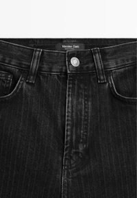 Black, herringbone-patterned denim jeans with a metal button, front pockets, and a branded label stitched at the waistband.