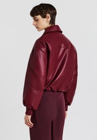 Giacca di pelle bordeaux con design imbottito, vestibilità oversize e colletto classico, abbinata a pantaloni a vita alta coordinati.