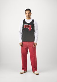 Fekete trikó Chicago Bulls logóval, piros egyenes szabású nadrággal és fekete akcentusokkal ellátott fehér sportcipőkkel párosítva.