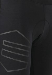 Svart träningsleggings tillverkade av stretchigt material, med en texturerad design och en cirkulär utskärning på sidan med en logografik.