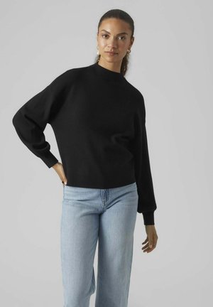 Zwarte gebreide trui met een hoge hals, een relaxte pasvorm en lange mouwen, gecombineerd met lichtblauwe wijde jeans. Glad textuur.