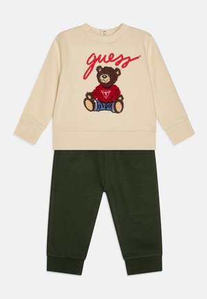 Felpa crema con design di un orso e la scritta "guess" in lettere rosse, abbinata a pantaloni verde scuro, entrambi realizzati in tessuto morbido.