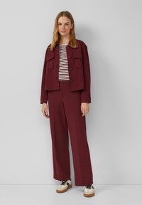 Bordeaux cropped jas met twee voorzakken, gedragen met een gestreept topje en wijde broek. Witte sneakers met zwarte accenten.