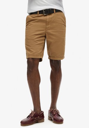 Pantalones cortos caqui con un ajuste casual, fabricados en algodón. Presentan bolsillos laterales, dobladillo cosido y un cinturón negro. Combinados con zapatos de barco burdeos.