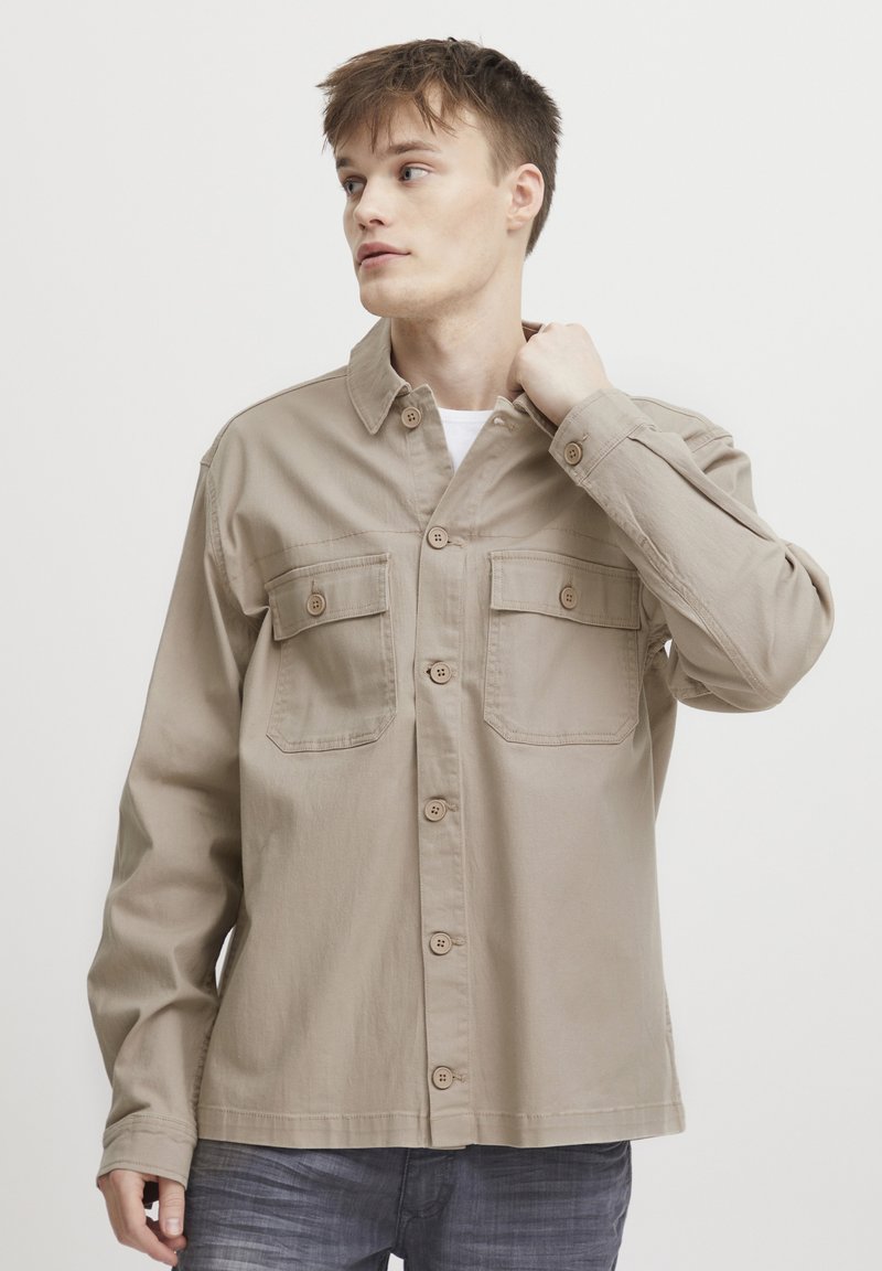 Beige langermet skjorte med knappestolpe, to brystlommer og krage. Laget av myk stoff med en avslappet passform.