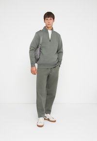 Grüner Baumwoll-Sweatshirt mit halbem Reißverschluss, kombiniert mit passenden Sweatpants und beigen Sneakers. Das Outfit zeichnet sich durch ein strukturiertes Design aus.