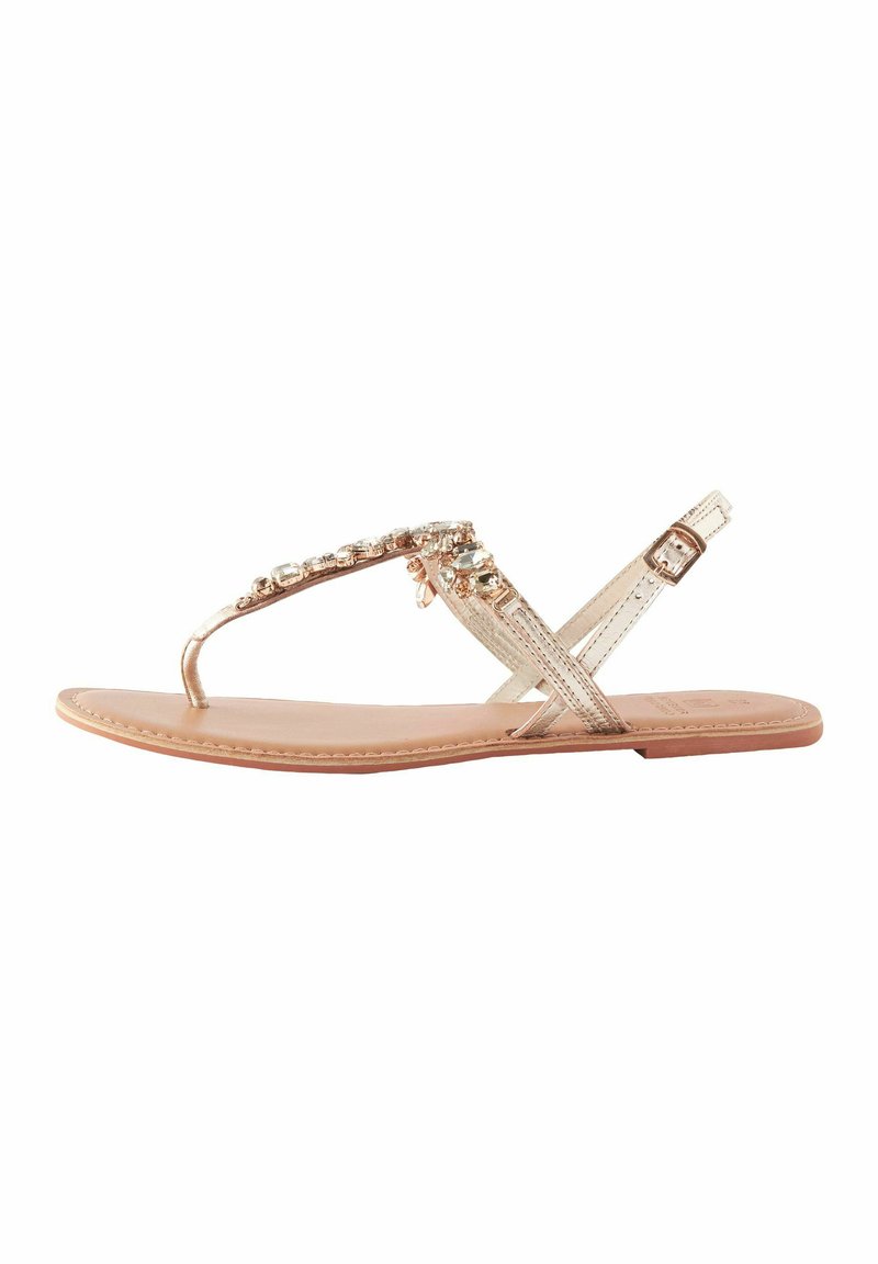 Platt sandal med metalliska remmar i guld, med klara pärlaccent längs ovandelen. Texturerat fotbädd och säker vristrem.